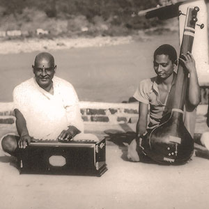 The Master playing harmonium, Swami Venkatesananda on the veena, and other musicans playing by the Ganges. 