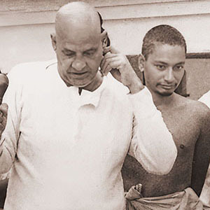 Visitor falls to ground to prostrate at the feet of Swami Sivananda while others including Swami Venkatesananda look on