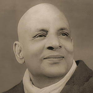 Swami Sivananda wears the enormous winter coat and scarf given to him by a devotee