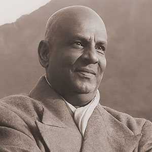 Swami Sivananda standing with arms folded overlooking the Ganges and Himalayan mountain range
