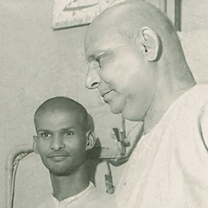 Swami Dayananda showing Swami Sivananda how he cuts the printed pages to size using the guillotine machine. 