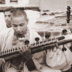 Swami Venkatesananda playing the veena for an outdoor kirtan while Gurudev Sivananda looks on. 