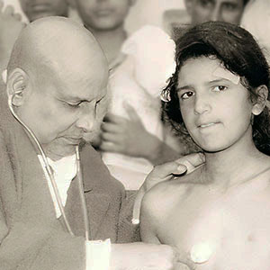 Swami Sivananda, listens to heart and lungs of young boy using a stethoscope