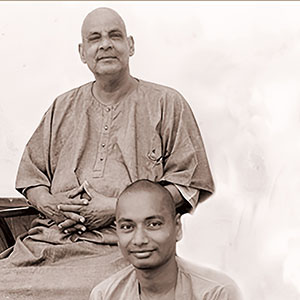Sivananda sitting in a chair with his disciple sitting on the ground in front of him, both facing and looking at the camera.