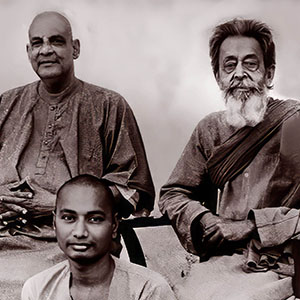 Sivananda and Achyutanand next to eachother on chairs with Swami Venkatesananda sitting on the floor in front of them. 